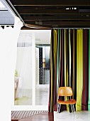Rooms forming a right angle around corner of courtyard with encircling boardwalk and mosquito curtains; classic Eames chair (LCM) against striped curtain