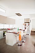 Barstools at free-standing counter in open-plan, white, designer kitchen