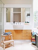 Large washstand with wooden doors, protruding sink and wide mirror; view through window above bathtub