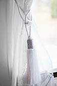 Classic, white cord tieback with tassel on curtain at window