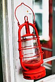 Old, red hurricane lamp hanging from white window frame