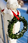 Box wreath hanging from red ribbon on snowy, vintage wooden post
