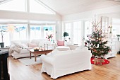 White sofa set and decorated Christmas tree in open-plan interior with rustic character