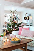 Scatter cushions on white sofa, rustic wooden coffee table and decorated Christmas tree in rustic living room