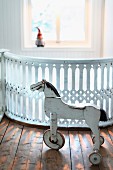 Vintage, white, wooden, three-wheeled horse in front of carved wooden balustrades painted white