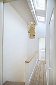 Narrow landing with wooden floor next to head of staircase and paper pendant lamp suspended from ceiling with skylights