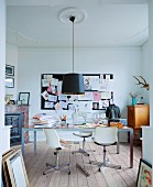Retro swivel chairs with white shell seats at modern table below pendant lamp with black lampshade suspended from stucco ceiling; pinboard on wall in background