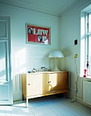 Mushroom-shaped lamp on wooden, fifties sideboard in corner against white-painted wooden wall