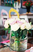 Bouquet of white and pale lilac roses in cylindrical glass vase; dining area in blurred background