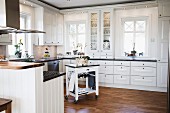 White fitted kitchen with encircling frieze, recessed lights and butchers' block trolley