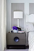 Grey bedside cabinet with drawers and white table lamp against wood-panelled bedroom wall
