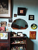 Offenes Regal aus dunklem Holz im Vintagestil an getönter Wand mit Bildern um halbkreisförmigem Spiegel