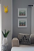 Scatter cushion printed with eye test chart on sofa, white-framed pictures and stylised, yellow rabbit hunting trophy on wall painted pale grey