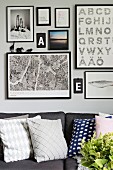 Gallery of framed pictures and typefaces above grey sofa with scatter cushions