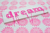 White-painted board with motto written in pink using threads wrapped around pins on fabric background with ornamental pattern