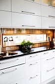 Modern fitted kitchen with white fronts and stainless steel handles; ribbon window with view in splashback area