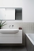 Ovales Waschbecken mit Wandarmatur auf Mosaikfliesen neben Badewanne