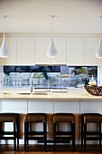White modern kitchen with pendant lamps and brown stools