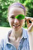 A young woman covering her eye with a leaf