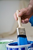 Person dipping a paintbrush into a paint tin