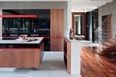 Ausschnitt eines offenen Kochbereiches, Küchenblock mit Holzunterschrank, oberhalb rote, Stab Hängeleuchte in modernem Ambiente