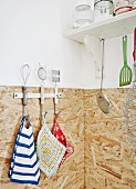 Hand-crocheted pot holders inherited from family and kitchen utensils hung on wall in corner of kitchen with chipboard splashback
