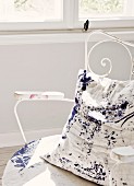 Cushion with blue splattered paint on white background on delicate, vintage metal chair painted white