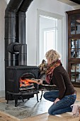 Woman putting firewood into wood-burning stove in rustic living room
