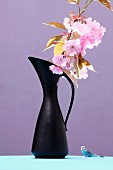 Branch of cherry blossom in black vase and budgerigar ornament against purple background