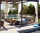 Roofed lounge area with outdoor furniture on wooden terrace in summer sun
