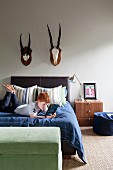 Boy reading on bed below two hunting trophies on wall