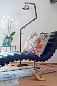 Designer couch with black leather cover and colourful scatter cushion in front of retro, stainless steel standard lamp
