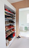 Open-plan, floor-to-ceiling shoe rack next to bathroom entrance with view of modern bathtub