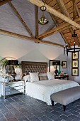 Double bed with button-tufted headboard in elegant, vintage bedroom with exposed roof structure