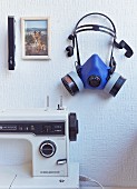 Detail of sewing machine below blue respirator mask and photo of dog on wall
