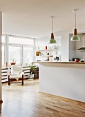 Kitchen counter below retro pendant lamps in open-plan, minimalist interior with armchair in front of window