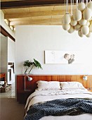 'Eggs' designer lamp and portrait artwork above modern bed with headboard in bedroom with ensuite bathroom in background