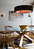 Ring-shaped pendant lamp above round table with solid wooden base and wooden armchairs on sisal rug