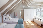 Guest bedroom with twin beds in bright attic room with white-painted wooden beams and parquet floor