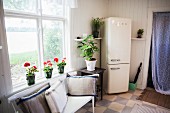 Simple bench with scatter cushions below window, red geraniums on windowsill and retro fridge-freezer