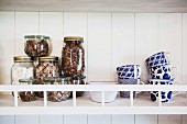 Storage jars and white and blue painted mugs on wall-mounted shelf