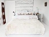 Fur blanket and bolster on double bed with carved wooden headboard against white horizontal boards on wall