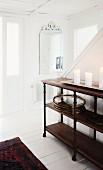 Candles on dark, half-height wooden shelves against staircase in white, wood-clad foyer