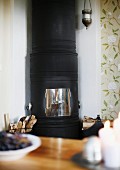 Blick über Tisch auf schwarzen, gusseisernen Kaminofen in Zimmerecke