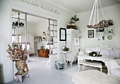 Ländlicher Wohnraum in Weiß, an Decke aufgehängter Kranz über Couchtisch, seitlich offener Durchgang mit Sprossen-Raumteiler und Blick ins Esszimmer