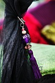 Oriental, purple tassel threaded with glass beads clipped to black mosquito net