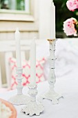 White candles in white, vintage candlesticks in romantic, outdoor setting