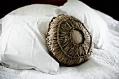 Cushion with ruched, brown-grey fabric cover amongst white pillows