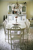 White dining set; chairs with seat covers around oval table below candle chandelier