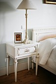 Table lamp on Regency-style bedside table painted white next to bed